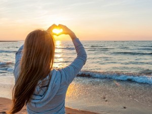 Girl holding hands in heart shape at beach