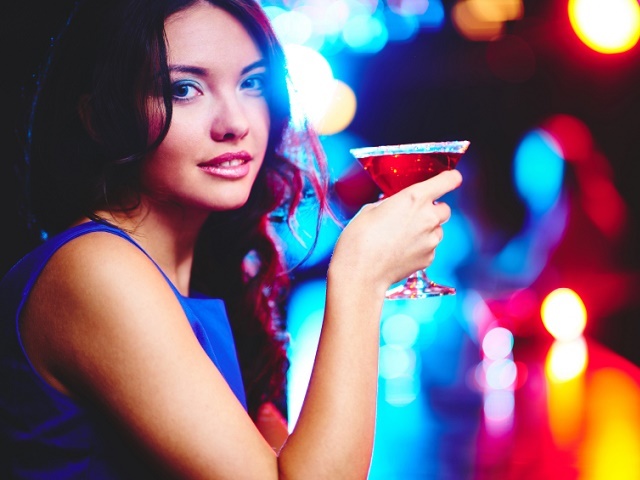 Pretty young girl with cocktail looking at camera on sparkling background