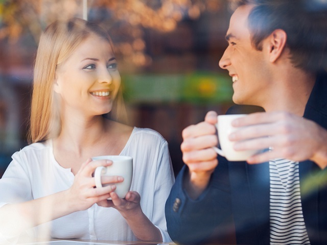 Enjoying fresh coffee together. Through a glass shot of beautiful young couple looking at each other and smiling while enjoying coffee in cafe together