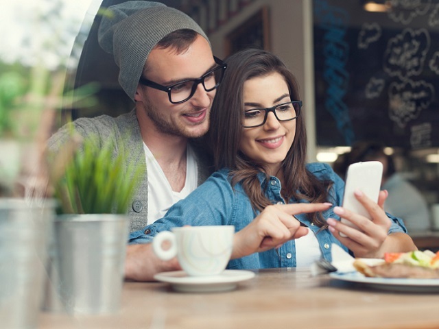 Embracing couple using mobile phone in cafe
