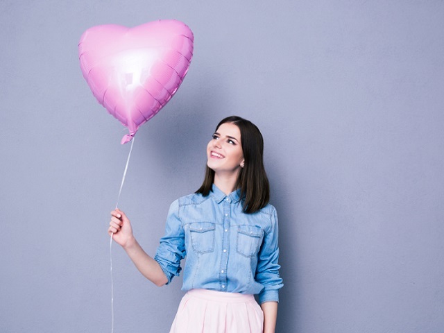 Happy woman holding balloon over gray background