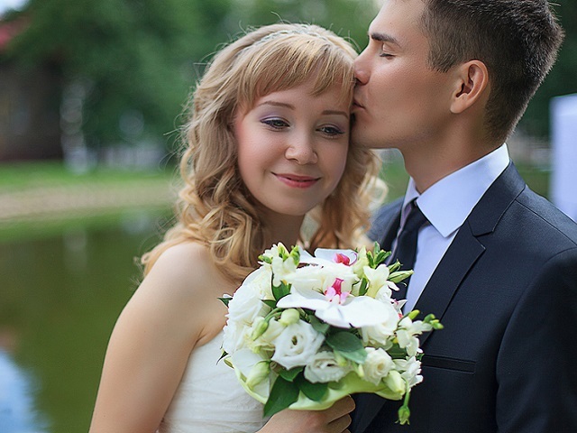 Groom gently kisses the bride on a background of lake